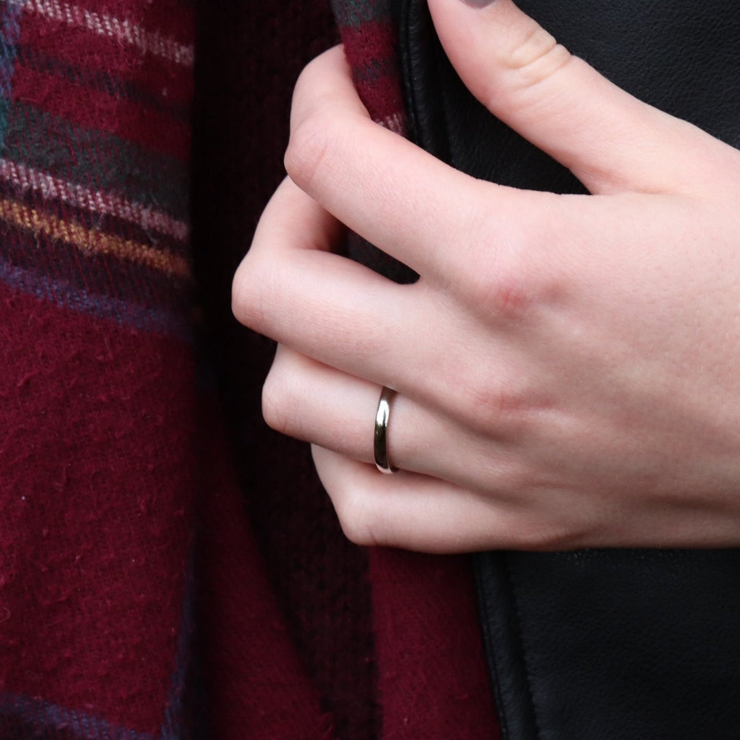 Slim polished Stainless Steel Wedding Ring on hand holding jacket and scarf.