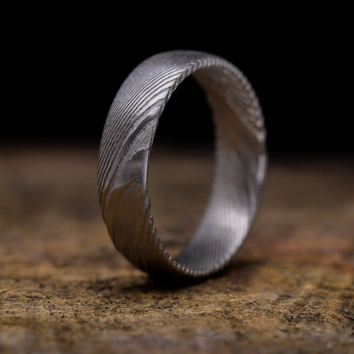 A Damascus Stainless Steel wedding ring with woodgrain effect pattern sits on top of a wooden surface.